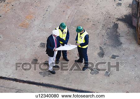 Stock Image - Workers reading blueprints at dry dock. Fotosearch