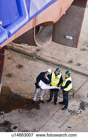 Stock Photo - Workers reading blueprints at dry dock. Fotosearch