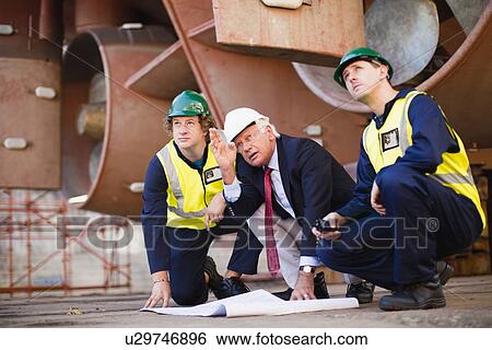 Stock Photograph - Workers reading blueprints on dry dock. Fotosearch