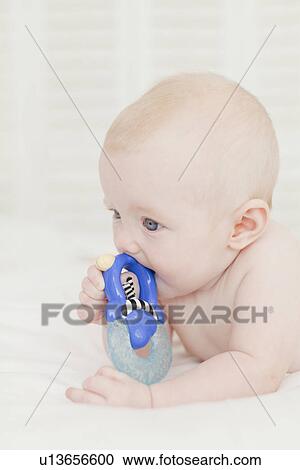 Stock Image - Baby chewing on rattle in bed. Fotosearch