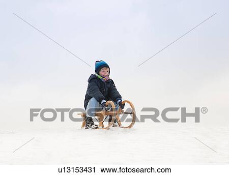 Stock Image - Boy sitting on sled in snow. Fotosearch
