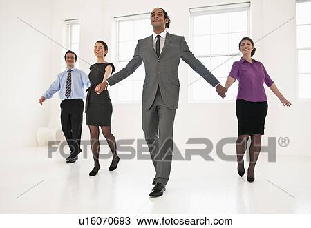 Stock Image - Business people holding hands in office. Fotosearch