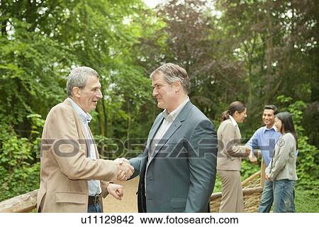 Stock Image - Businessmen shaking hands in forest. Fotosearch