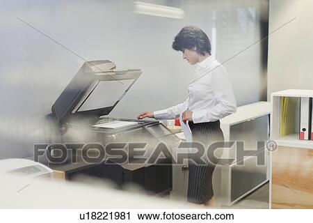 Stock Image - Businesswoman making copies in office. Fotosearch