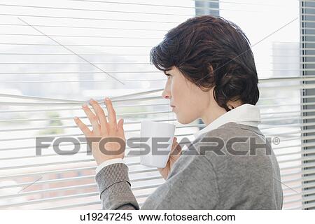 Businesswoman peering out office window View Large Photo Image Stock Photography - Businesswoman peering out office window. Fotosearch