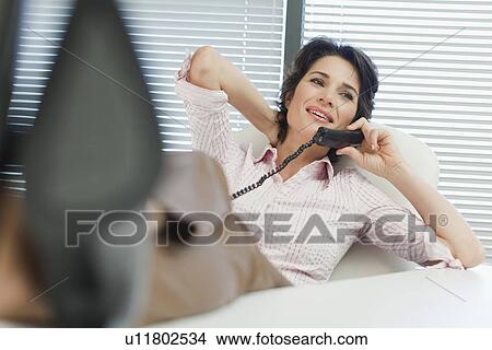 Picture - Businesswoman talking on phone at desk. Fotosearch
