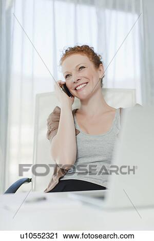 Stock Image - Businesswoman talking on phone at desk. Fotosearch