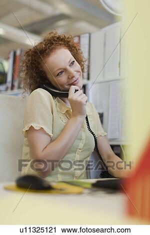 Stock Image - Businesswoman talking on phone at desk. Fotosearch