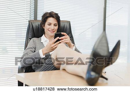 Businesswomen using cell phone at desk View Large Photo Image Stock Photo - Businesswomen using cell phone at desk. Fotosearch