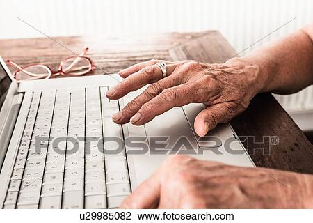 Stock Image - Close up of older mans hands on laptop. Fotosearch