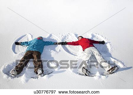 Couple making snow angels outdoors View Large Photo Image Stock Photo - Couple making snow angels outdoors. Fotosearch
