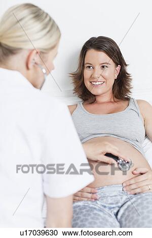 Stock Image - Doctor examining pregnant womans belly. Fotosearch