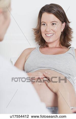 Stock Image - Doctor examining pregnant womans belly. Fotosearch
