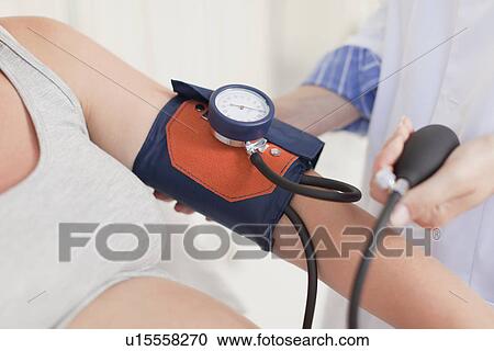 Stock Image - Doctor taking womans blood pressure. Fotosearch