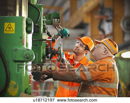 Stock Photo - Engineer teaching apprentice in factory. Fotosearch