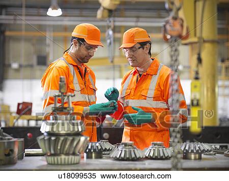 Stock Photography - Engineer teaching apprentice in factory. Fotosearch