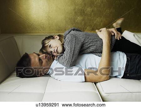Stock Image - Father and daughter relaxing on sofa. Fotosearch