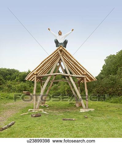 Stock Photo - Man cheering on roof of log hut. Fotosearch