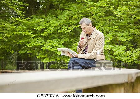Stock Photograph - Man reading newspaper in park. Fotosearch