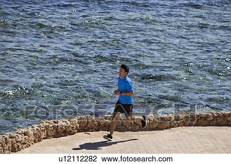 Stock Image - Man running on paved coastline. Fotosearch