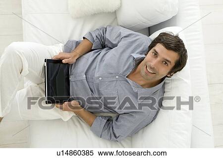 Stock Photography - Man using tablet computer on sofa. Fotosearch