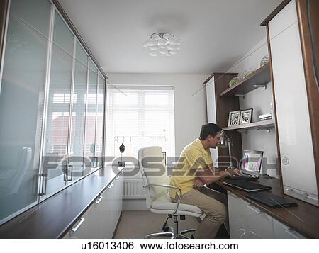 Man working on laptop in home office View Large Photo Image Stock Photograph - Man working on laptop in home office. Fotosearch