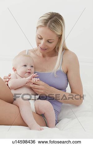 Stock Photograph - Mother and baby sitting on bed. Fotosearch