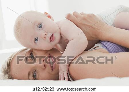 Stock Image - Mother hugging baby on bed. Fotosearch