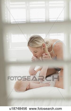 Stock Photograph - Mother kissing babys feet on bed. Fotosearch