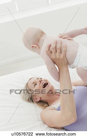 Stock Image - Mother playing with baby on bed. Fotosearch