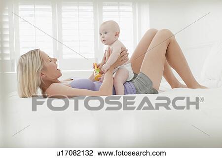 Stock Image - Mother playing with baby on bed. Fotosearch