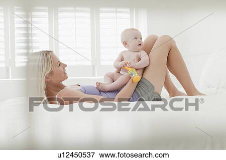 Stock Photo - Mother playing with baby on bed. Fotosearch