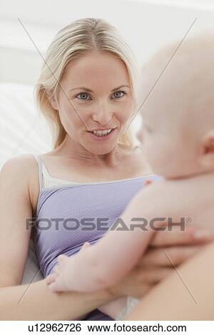 Stock Photograph - Mother playing with baby on bed. Fotosearch