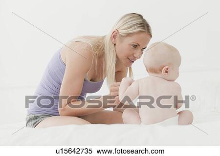 Stock Photography - Mother playing with baby on bed. Fotosearch