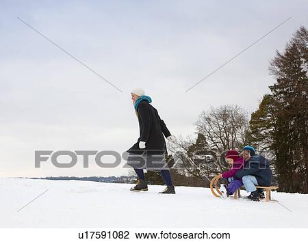 Stock Image - Mother pulling children on sled in snow. Fotosearch