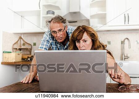 Picture - Older couple using laptop in kitchen. Fotosearch