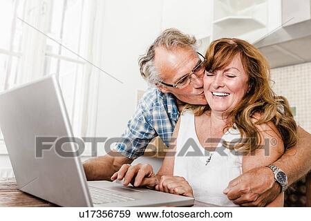 Stock Photo - Older couple using laptop in kitchen. Fotosearch
