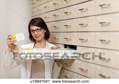 Stock Image - Pharmacist browsing medicine in drawer. Fotosearch