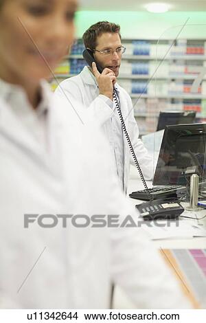 Pharmacist talking on phone at counter View Large Photo Image Picture - Pharmacist talking on phone at counter. Fotosearch