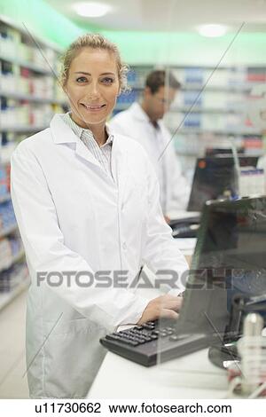 Stock Image - Pharmacist using computer at counter. Fotosearch