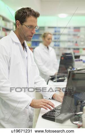Pharmacist using computer at counter View Large Photo Image Stock Image - Pharmacist using computer at counter. Fotosearch