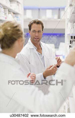 Stock Image - Pharmacists browsing medicines on shelf. Fotosearch