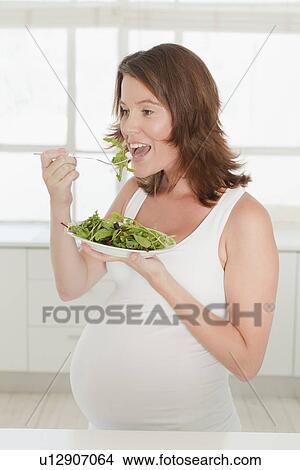 Pregnant woman eating salad in kitchen View Large Photo Image Picture - Pregnant woman eating salad in kitchen. Fotosearch