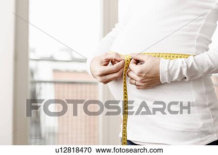 Stock Image - Pregnant woman measuring her belly. Fotosearch