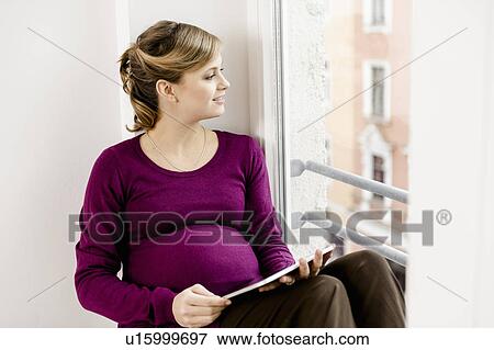 Stock Photo - Pregnant woman sitting in window. Fotosearch