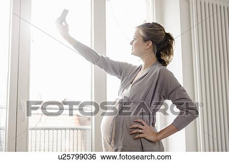 Stock Photograph - Pregnant woman taking picture of herself. Fotosearch