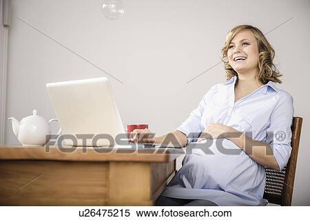 Stock Photography - Pregnant woman using laptop in kitchen. Fotosearch