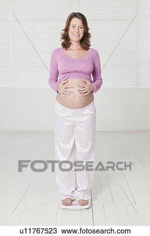 Stock Image - Pregnant woman weighing herself. Fotosearch