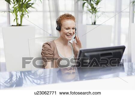 Stock Image - Receptionist wearing headset at desk. Fotosearch
