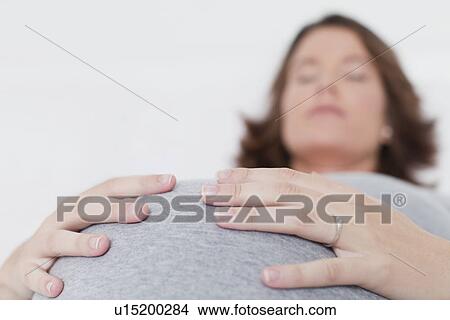 Picture - Sleeping woman holding pregnant belly. Fotosearch